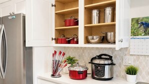 Una cocina con un refrigerador de acero inoxidable, una olla de cocción lenta roja, una olla eléctrica negra a presión y varios utensilios en la encimera.