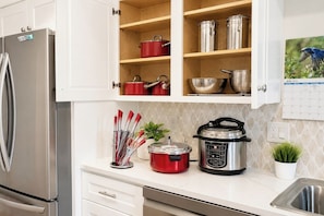 A kitchen with a stainless steel refrigerator, a red slow cooker, a black electric pressure cooker, and various utensils on the counter.