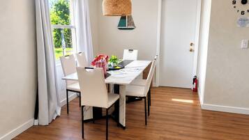 A dining area with a table, chairs, a hanging light fixture, a door, and a wall clock.
