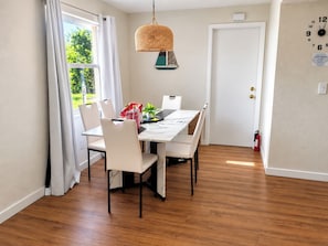 Un comedor con una mesa, sillas, una lámpara colgante, una puerta y un reloj de pared.