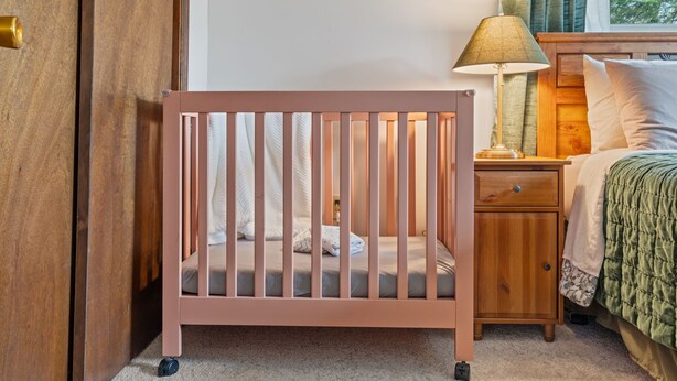 Een babybed met houten frame en een klein nachtkastje met lamp.