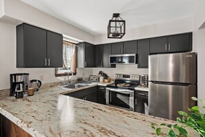 A modern kitchen with dark cabinets, stainless steel appliances, a marble countertop, and a hanging light fixture. - Campfire Nights Start Here. Fireplace, Game Loft & Fall Adventures (Blakeslee)