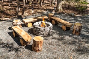 A fire pit surrounded by wooden benches and logs in a forest setting. - Where Fall Memories Are Made! Hiking, Campfire Nights, Games, Cozy Fireplace (Blakeslee)