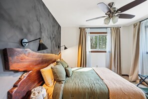 A bedroom with a large wooden headboard, a ceiling fan, and a view of the outdoors through a window. - Campfire Nights Start Here. Fireplace, Game Loft & Fall Adventures (Blakeslee)
