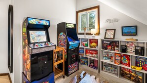 Een kamer met twee speelautomaten, een raam met uitzicht en planken vol spelletjes.
