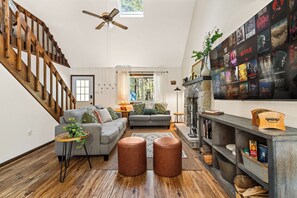 A spacious living room with a wooden staircase, a fireplace, and a wall of movie posters. - Campfire Nights Start Here. Fireplace, Game Loft & Fall Adventures (Blakeslee)