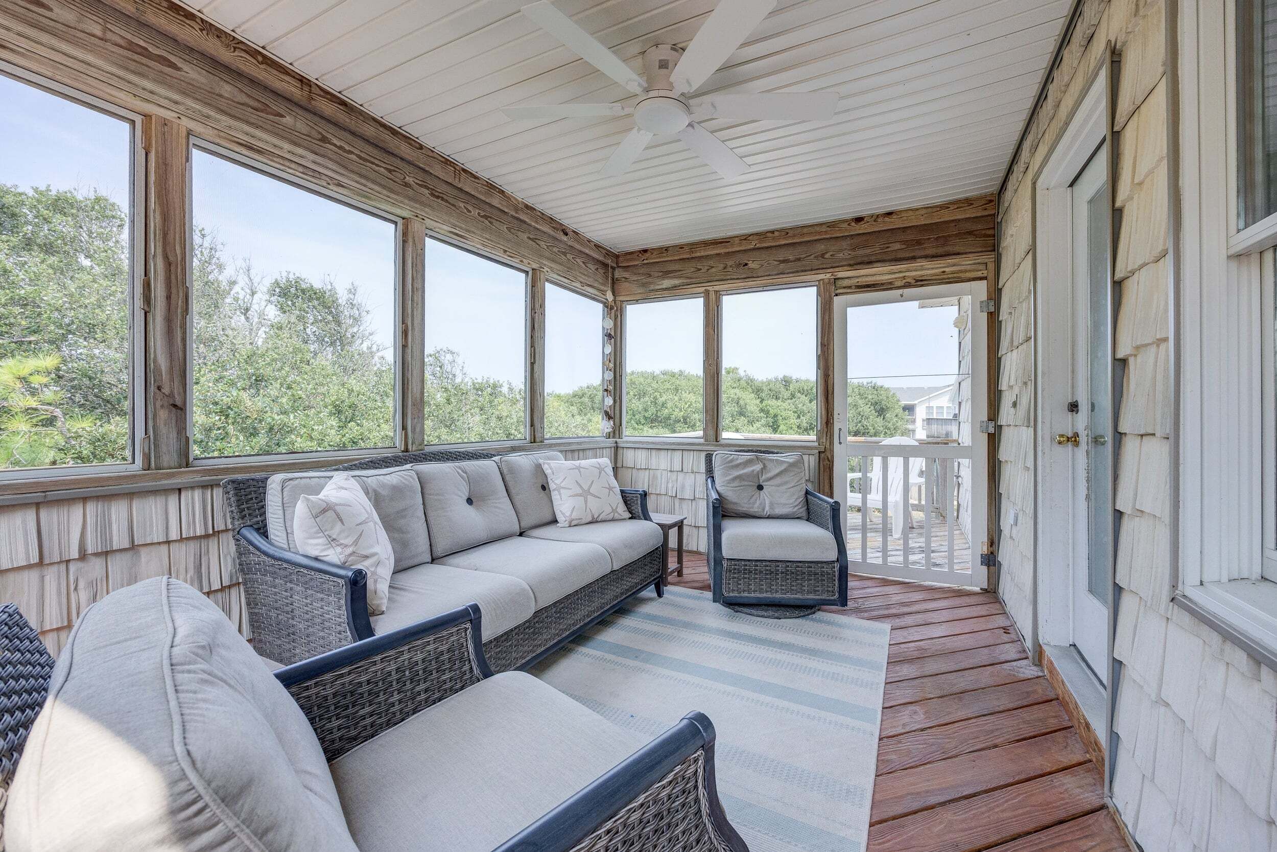 A covered porch with wicker furniture, a ceiling fan, and large windows offering a view of the outdoors.