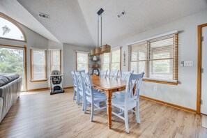 A spacious dining area with a wooden table and white chairs, large windows with blinds, and a ceiling with recessed lighting. - 1615 - Smallfield Shores - Oceanside Corolla retreat with 4 bedrooms, ocean view, pool, hot tub. (Corolla)