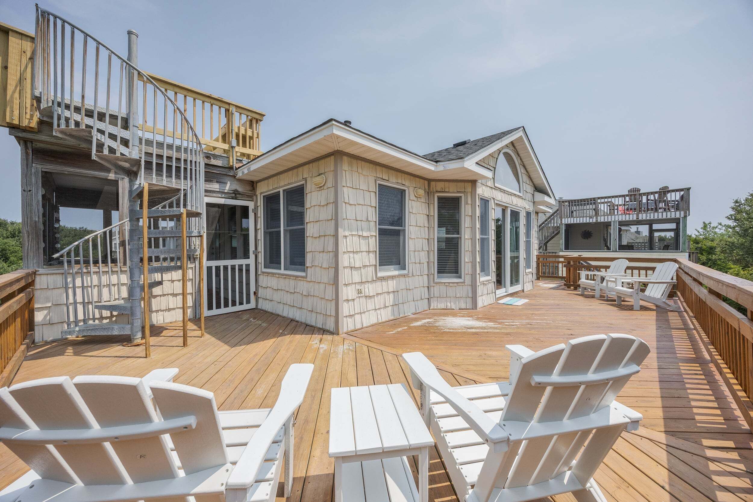A wooden deck with Adirondack chairs, a staircase, and a house with large windows.