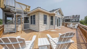Una terrazza in legno con poltrone Adirondack, una scala e una casa con ampie finestre.