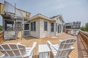 A wooden deck with Adirondack chairs, a staircase, and a house with large windows. - 1615 - Smallfield Shores - Oceanside Corolla retreat with 4 bedrooms, ocean view, pool, hot tub. (Corolla)