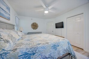 A bedroom with a bed, a ceiling fan, a wall-mounted TV, and a door. - 1615 - Smallfield Shores - Oceanside Corolla retreat with 4 bedrooms, ocean view, pool, hot tub. (Corolla)