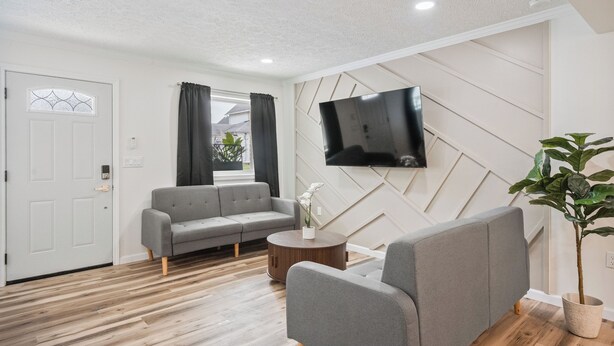Un salón moderno con un sofá gris, un televisor de pantalla plana montado en la pared y una planta en maceta.