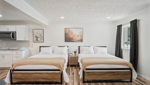 Habitación de hotel con dos camas, kitchenette y un amplio ventanal con cortinas.