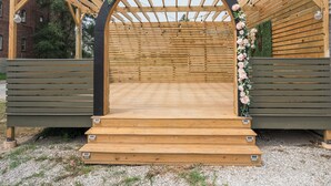Un arco de madera con un arreglo floral, que conduce a una zona de estar con bancos.
