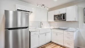 Una cocina moderna con armarios blancos, un refrigerador de acero inoxidable, un microondas y piso de madera.