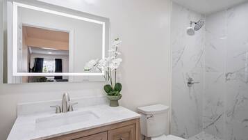 A modern bathroom with a marble sink, wooden cabinets, a toilet, and a shower with a glass door.