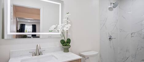 Un baño moderno con lavamanos de mármol, armarios de madera, inodoro y ducha con puerta de vidrio.