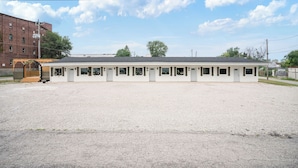 A single-story motel with a gravel driveway and a brick building in the background. - Clair de Lune Studio A Charming Kokomo Stay (Kokomo)