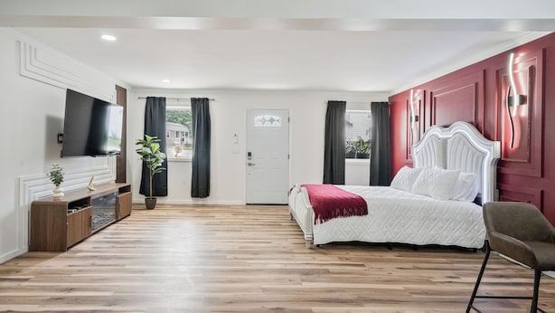 A bedroom with a bed, a TV, a plant, and a wooden floor. - Clair de Lune Studio A Charming Kokomo Stay (Kokomo)