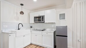 A kitchen with white cabinets, a stainless steel refrigerator, a microwave, and a sink with a faucet. - Clair de Lune Studio A Charming Kokomo Stay (Kokomo)