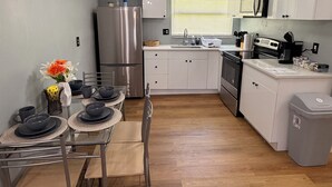 A modern kitchen with stainless steel appliances, a dining area with a glass table, and a grey trash bin. - Stylish 2-bedroom apartment with AC in near FLL airport & Hollywood beach (Hollywood)