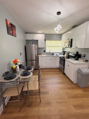 A modern kitchen with stainless steel appliances, a dining area with a glass table, and a grey trash bin. - Stylish 2-bedroom apartment with AC in near FLL airport & Hollywood beach (Hollywood)
