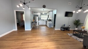 A spacious living room with a wooden floor, a dining area with a table and chairs, a kitchen with modern appliances, and a ceiling fan. - Stylish 2-bedroom apartment with AC in near FLL airport & Hollywood beach (Hollywood)