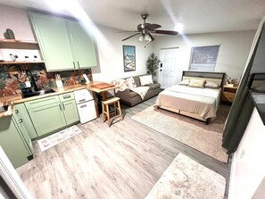 Ein kompakter Wohnraum mit Küchenzeile, einem Bett, einem Deckenventilator und einem Fenster mit Jalousien.