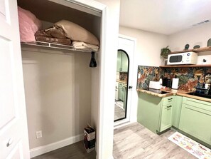 A compact kitchen with a microwave, a toaster, and a sink. There is a small cabinet and a door leading to another room.