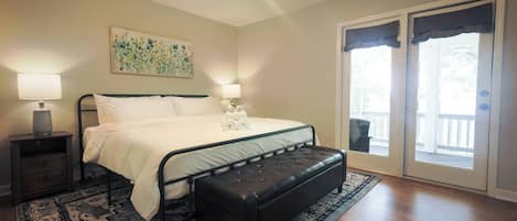 A bedroom with a bed, bedside tables, a bench, a ceiling fan, a painting, and a sliding glass door leading to an outdoor area.