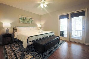 Ein Schlafzimmer mit einem Bett, Nachttischen, einer Bank, einem Deckenventilator, einem Gemälde und einer Schiebetür zu einem Außenbereich.