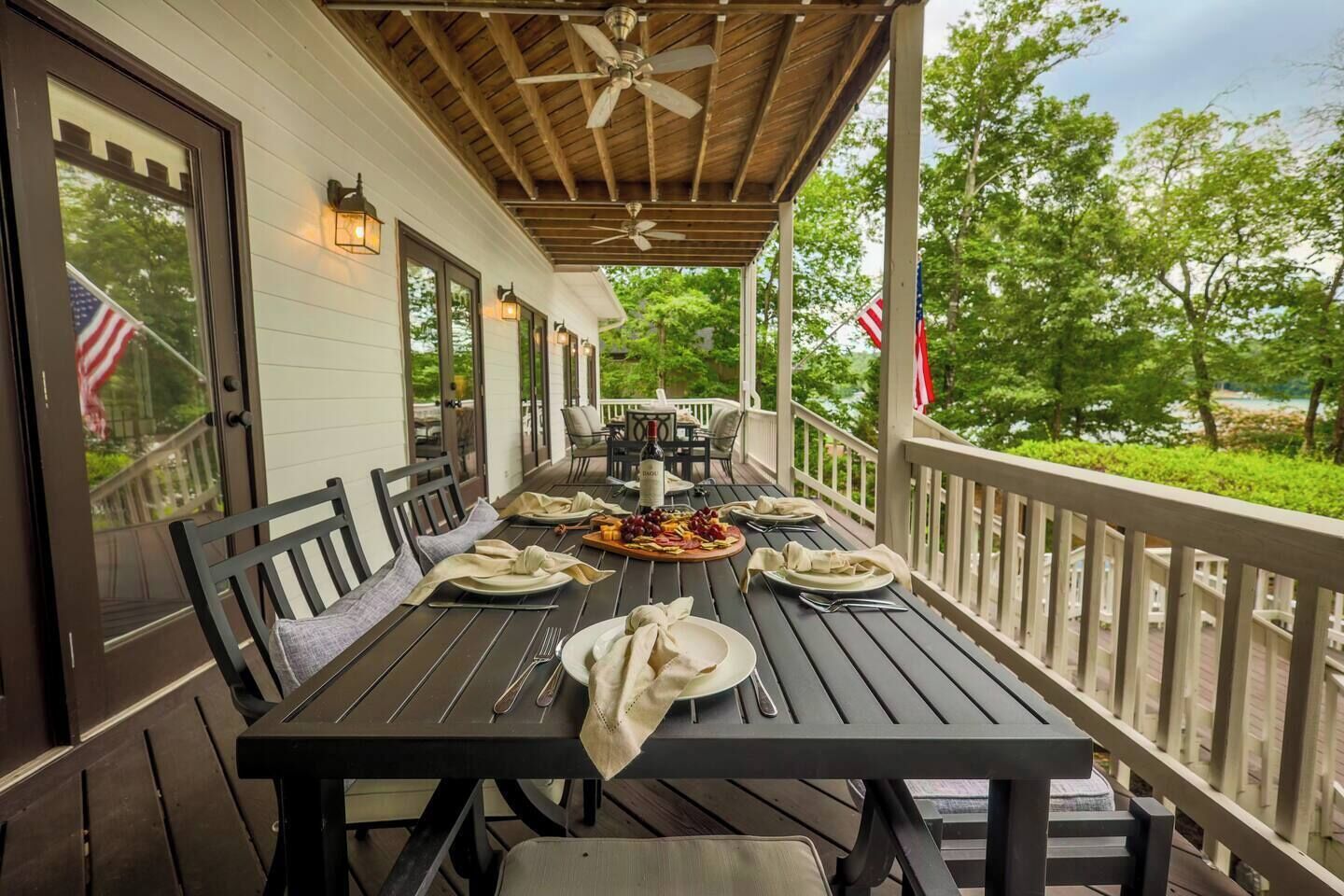 A covered outdoor dining area with a table set for four, surrounded by chairs, and a view of greenery.