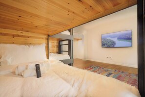 Une chambre à coucher avec un lit, une télécommande, un tableau au mur et une fenêtre.