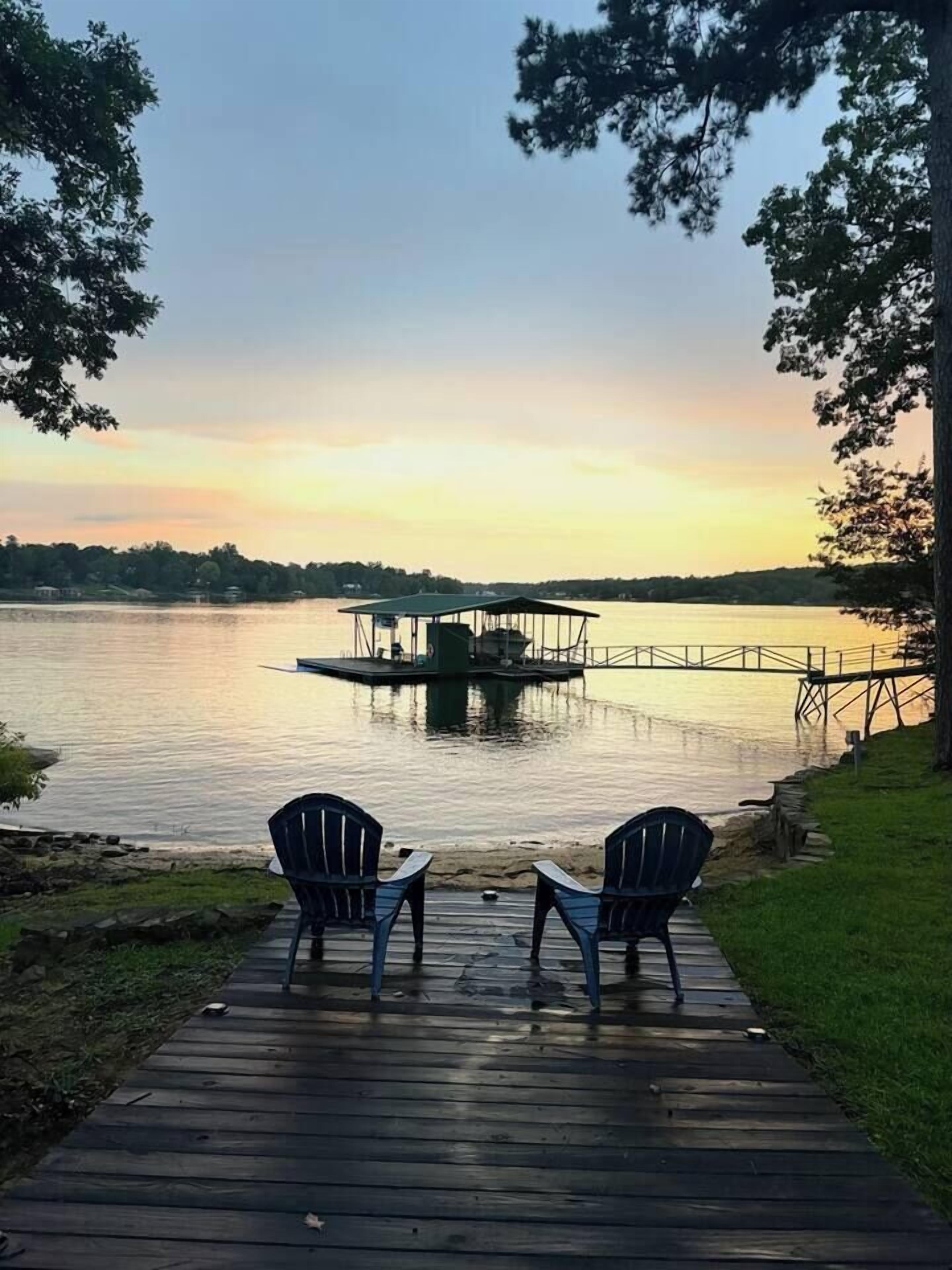 Une jetée en bois avec deux chaises, donnant sur un lac paisible au coucher du soleil.
