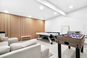A modern living room with a foosball table, a pool table, and a sofa. - Fun & Modern Summer Pool Home near Disney! (Anaheim)