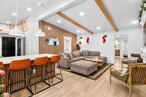 A modern living room with a sectional sofa, ottoman, and bar stools. - Fun & Modern Summer Pool Home near Disney! (Anaheim)