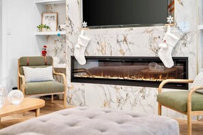 A modern living room with a fireplace, two armchairs, a coffee table, and a television. - Fun & Modern Summer Pool Home near Disney! (Anaheim)