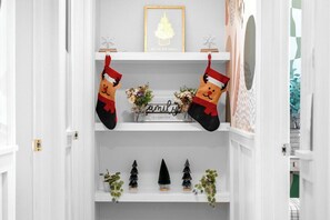 A hallway with a white door, a framed picture on the wall, and a shelf with small Christmas trees and a sign that reads 'family is forever.' - Fun & Modern Summer Pool Home near Disney! (Anaheim)