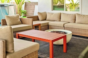 A cozy outdoor seating area with wicker furniture and a red table. - Fun & Modern Summer Pool Home near Disney! (Anaheim)