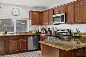 A modern kitchen with wooden cabinets, stainless steel appliances, and a granite countertop. - San Diego Pool Home Oasis with Backyard Retreat (San Diego)