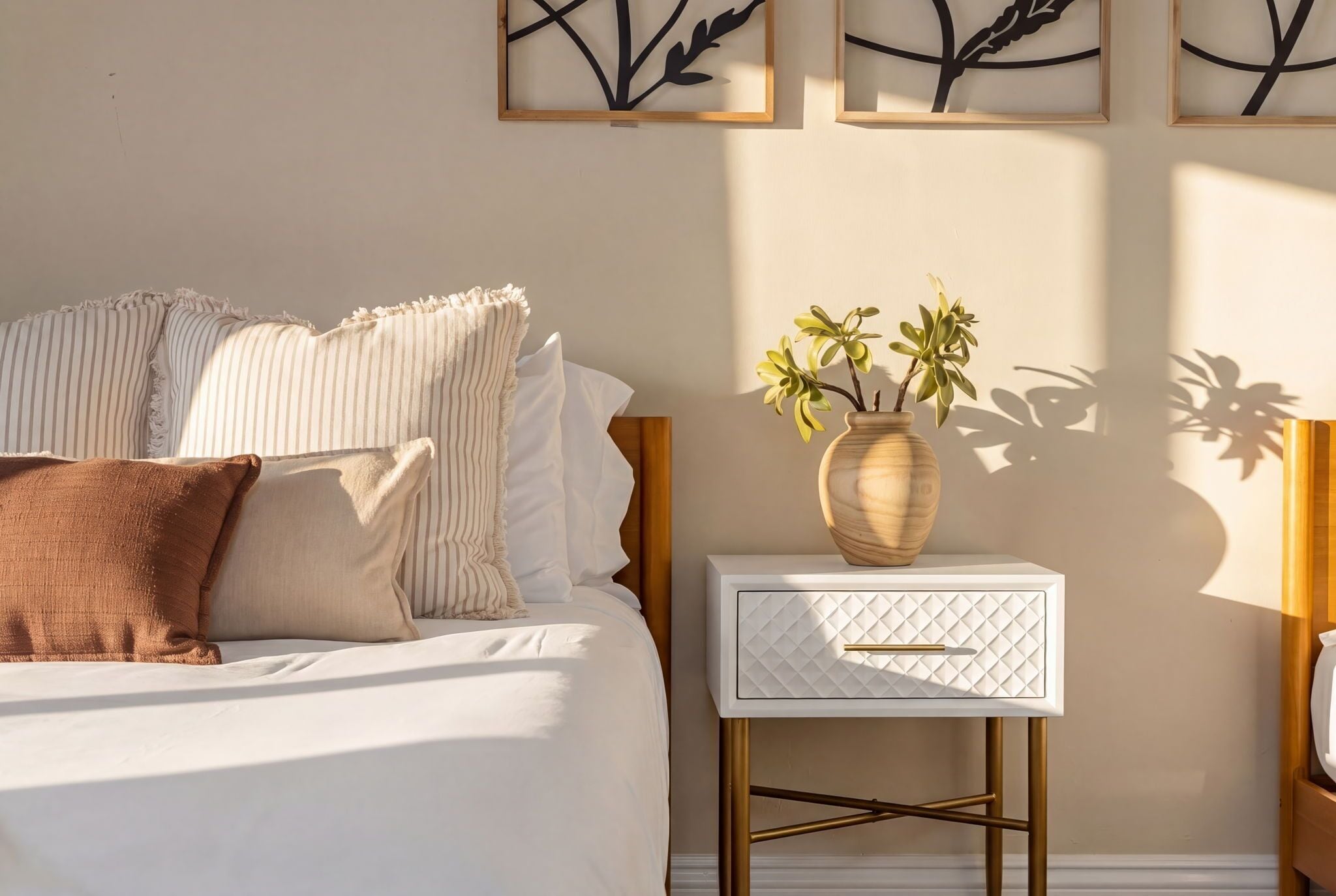 A bedroom with a bed, pillows, a bedside table with a vase of flowers, and wall art.