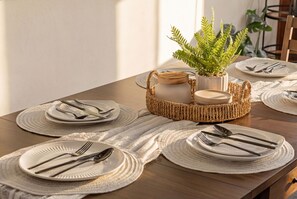 Une table à manger dressée avec de l’assiette blanche, des couverts en argent et des sets de table en fibres tressées.