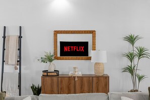 Ein Wohnzimmer mit einem Holzkabinett, einem an der Wand montierten Fernseher der Marke NETFLIX, einer Lampe und einem Blumentopf.