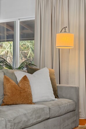 Un canapé gris avec trois coussins, un lampadaire et une fenêtre avec des rideaux.