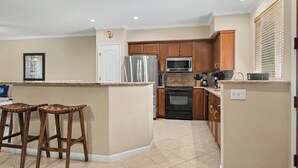 A kitchen with a central island, wooden cabinets, stainless steel appliances, and a tiled floor. - Walk to the Beach, Shopping, and Dining. (Waikoloa Village)