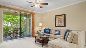 A living room with a beige couch, a glass coffee table, and a ceiling fan. - Walk to the Beach, Shopping, and Dining. (Waikoloa Village)