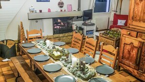 A dining area with a long wooden table set for a meal, a fireplace, and a television mounted on the wall. - 4 bedroom nice home in Binic (Binic)