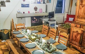 Ein Essbereich mit einem langen Holztisch, der für eine Mahlzeit gedeckt ist, einem Kamin und einem an der Wand befestigten Fernseher.