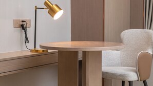 A round wooden table with a chair, a desk, and a lamp with a cord.